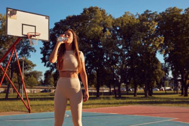 Şehir parkında koşudan ve egzersizden sonra su içen genç bir kadın.