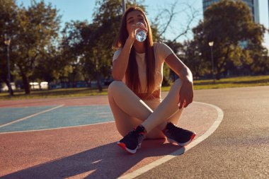 Şehir parkında koşudan ve egzersizden sonra su içen genç bir kadın.