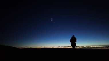 Ay 'ı, gezegenleri ve Samanyolu' nu karanlık bir kırsaldan izleyen bir kadının silueti..