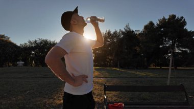 Gün batımında parkta koştuktan sonra susamış adam su içiyor..