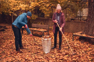 Kadın ve erkek, düşen sonbahar yapraklarından bahçeyi temizliyorlar..