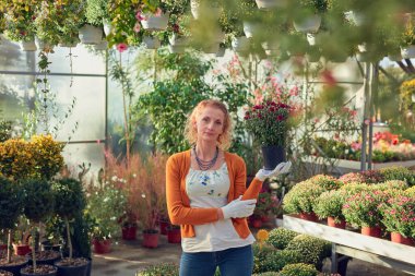 Çiçek yetiştirme yurdunda çalışan bir kadın, bitkilerle ilgileniyor ve onu satmak için hazırlıyor..