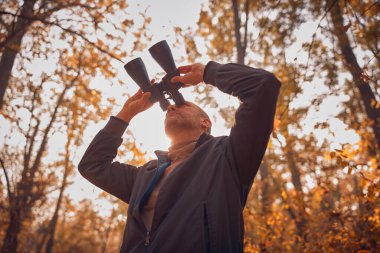 Kuşları ve diğer hayvanları dürbünle gözlemleyen amatör kuş gözlemcisi..