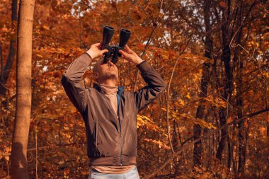 Kuşları ve diğer hayvanları dürbünle gözlemleyen amatör kuş gözlemcisi..