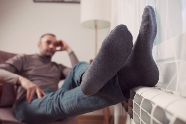 Soğuk bir kış gününde evin ısıtıcı kaloriferinde çoraplı bir adamın ayakları..