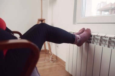 Soğuk bir kış gününde ev ısıtıcı radyatörde çoraplı bir kadının ayakları..