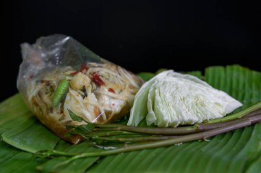Tayland yemeği olarak adlandırılan papaya salatası, salamura balık, plastik torbada tuzlanmış yumurta ve muz yaprağında sebze, yeşil, siyah arka plan