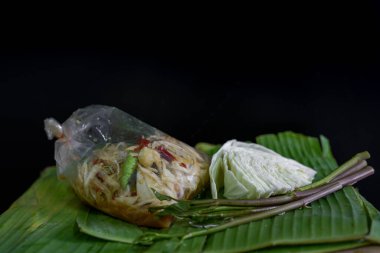 Tayland yemeği olarak adlandırılan papaya salatası, salamura balık, plastik torbada tuzlanmış yumurta ve muz yaprağında sebze, yeşil, siyah arka plan