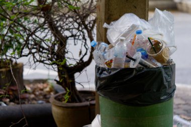 Dışarıdan taşan çöplerle dolu plastik çöp resmi.