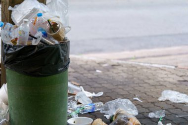 Dışarıdan taşan çöplerle dolu plastik çöp resmi.