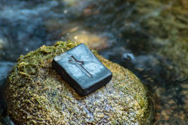 Norse rune Nautiz (Naud) on the stone and the evening river background.  Obstacles, the necessary awareness of difficulties and opportunities to overcome them. Strong bond, obligations. clipart