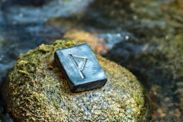 Norse rune Thurisaz (Thurs) on the stone and the evening river background. The strength and defense of a warrior. Male sexuality. Courage. Runa Thurisaz is associated with the Scandinavian God Thor.