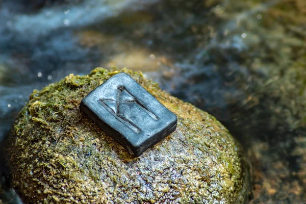 Norse rune Mannaz on the stone and the evening river background. Humanity, the development of the best human qualities. Self-realization. Work with human resources.