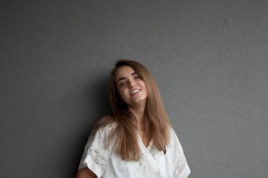 Kar beyazı gülümseyen ve mavi gözlü genç ve güzel bir kız. Kızın kafası hafifçe eğilmiş. Kız etrafında gri bir arka plan ve metin veya grafik için alan var.