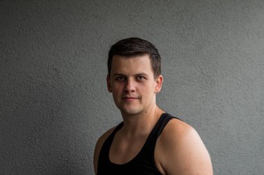 Genç, güçlü adam. Sakin bir görünüm ve hafif bir gülümseme. Gri arka plan.