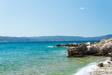 Deniz manzarası: kayalık kıyı, taşlar, sakin turkuaz su, mavi gökyüzü. Krk, Krk adası, Hırvatistan.