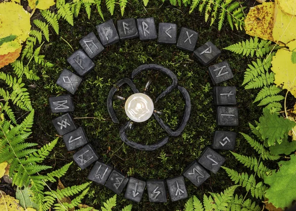 Ein Kreis aus 24 skandinavischen Runen auf dem Hintergrund von Moos und Blättern im herbstlichen Wald. in der Mitte des Kreises befindet sich ein geschmiedeter Kerzenständer mit einer Kerze. — Stockfoto