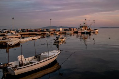 Hırvatistan'da balıkçı teknelerinin olduğu küçük bir liman, güneş batarken, mavi ve mor arka plan