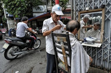 Hanoi, Vietnam - August 28: Barber shaving a man at the street on August 28, 2018 in Hanoi. clipart