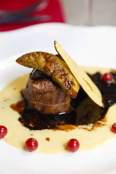 Grilled meat with a complex sauce, red currants, a slice of pear