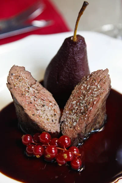 Grilled meat with a complex sauce, red currants, a slice of pear