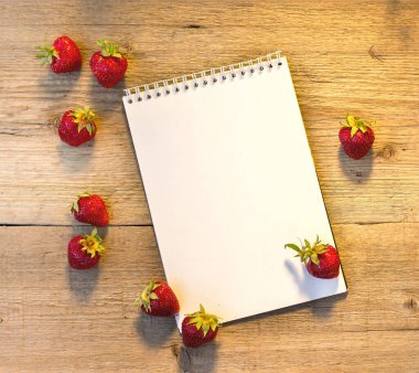 Ahşap arka planda parlak kırmızı olgun çilekler ve yazmak için bir kağıt için arkaplan