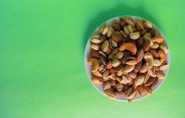 Kopya alanı ile yeşil arka plan üzerinde izole beyaz plaka üzerinde karışık fındık. Sağlıklı atıştırmalık ve yiyecek. Tuzlu ve baharatlı antep fıstığı, kaju ve badem. Üstte görüntü.