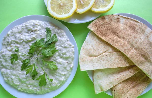 Famous traditional Arabic cuisine - dip Baba ganoush with pita bread and fresh lemon on green background. Flat lay, top view. Baba ganoush.