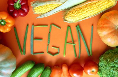 Turuncu arka plan üzerinde vegan kelime ile taze sebze Çerçeve. Yeşil soğandan yapılmış vegan kelime. Çeşitli sebzeler 