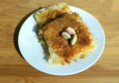 Geleneksel Orta Doğu tatlı kunafası. Üst Manzara. Beyaz tabakta bej ahşap masada peynirli konafa. Kunafa. 