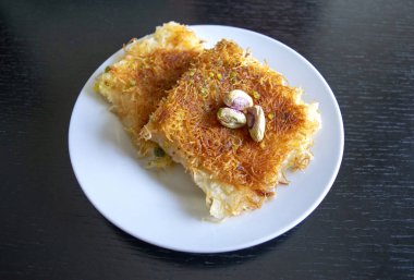 Geleneksel doğu tatlısı kunafa. Üst Manzara. Siyah ahşap masada beyaz tabakta Arap peynirli kunafa. Konafa. 