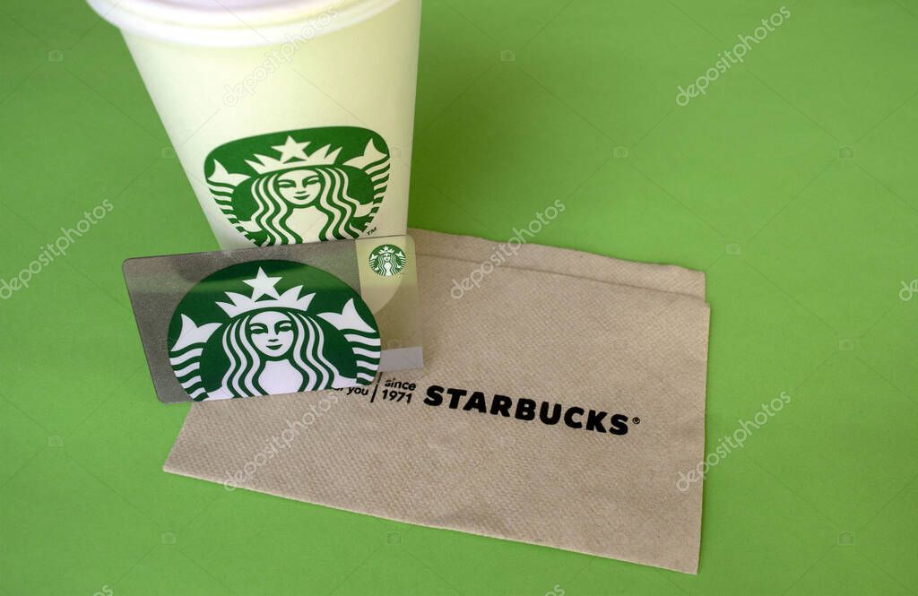 Dubai / UAE - June 7, 2020: Starbucks white coffee cup with gift card and napkin on green background with copy space