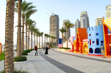 Dubai / BAE - 19 Haziran 2020: Dubai Creek Limanı, güzel kuleleri, yeşil palmiyeleri ve çocuk parkı olan yürüyüş / gezinti alanı. Dubai 'nin yeni ve güzel manzarası. 