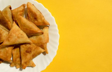 Ünlü geleneksel Arapça, Orta Doğu, Asya mutfağı. Sarı arkaplanlı ve fotokopi alanı olan üçlü Arap tavuklu samosa. Beyaz tabakta bir sürü lezzetli mini samsa