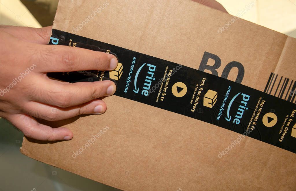 Dubai - UAE - July 04, 2020:  Man is opening cardboard box parcel of Amazon. Amazon prime free delivery package.