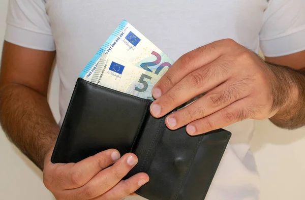 European Union currency. Euro money banknotes. Man in white t shirt put euro banknotes into black wallet. Young man holds in hands wallet with European paper money.