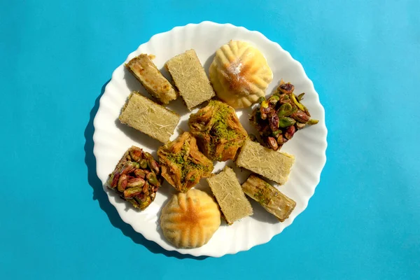 Biscuits traditionnels au mamoul du Moyen-Orient et baklawa assortis. Vue de dessus. Bonbons arabes cuits au four avec des noix dans une assiette blanche sur fond bleu. Ayd El Fithr biscuits de fête. — Photo