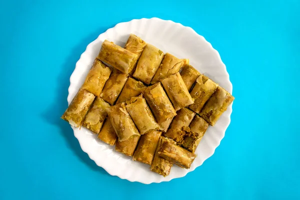 Традиционная турецкая, арабская, ближневосточная пахлава. Вид сверху. Арабская выпечка сладостей в белой тарелке на синем ярком фоне. Баклава, Мини — стоковое фото