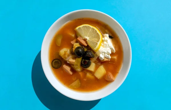 Solyanka soup in a white bowl on blue background. Top view. Famous traditional Ukrainian and Russian saltwort soup with lemon. — Stock Image Solyanka Soup White Bowl Blue Background Top View Famous Traditional Royalty Free Stock Images
