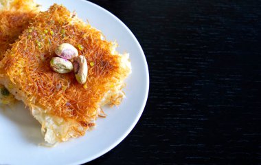 Geleneksel doğu tatlısı kunafa. Üst Manzara. Beyaz tabakta, siyah ahşap masada, kopyalama alanı olan Arap peyniri kunafa. Konafa.