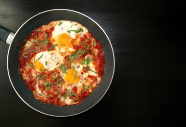 Shakshuka - domates soslu haşlanmış yumurta, soğan, biber ve baharatlar siyah ahşap masada, fotokopi alanı ile. Ünlü geleneksel Arapça ve İsrail kahvaltısı, Chakchouka. Üst görünüm.