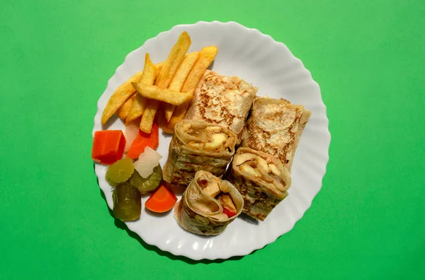 Известная традиционная арабская, ближневосточная, израильская кухня. Арабская тарелка шаурмы с жареной картошкой и маринованными овощами на зеленом фоне. Квартира лежала, вид сверху. Обертка шаурмы на белой тарелке — стоковое фото