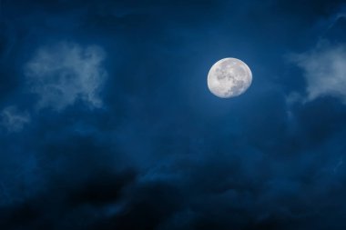 Moon at night with bright and dark clouds on blue background clipart