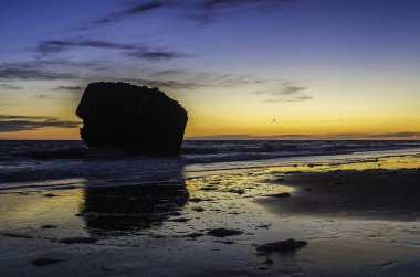 su içinde kaya gözetleme kulesi ve kıyı nın su yansımaları ile sahilde mavi ve turuncu gün batımı