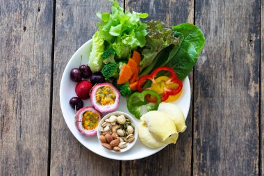 Ahşap bir masada beyaz bir tabak üzerinde Meyve ve Sebze salatası