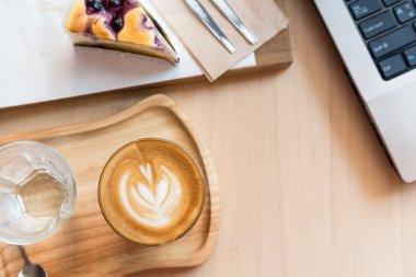 bir kahve dükkanında ahşap bir masada kek ve dizüstü bilgisayar ile kahve fincanı latte sanat. 