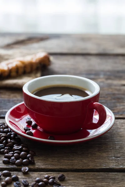 Κόκκινο φλιτζάνι καφέ και φασόλια καφέ σε ξύλινο φόντο — Φωτογραφία Αρχείου