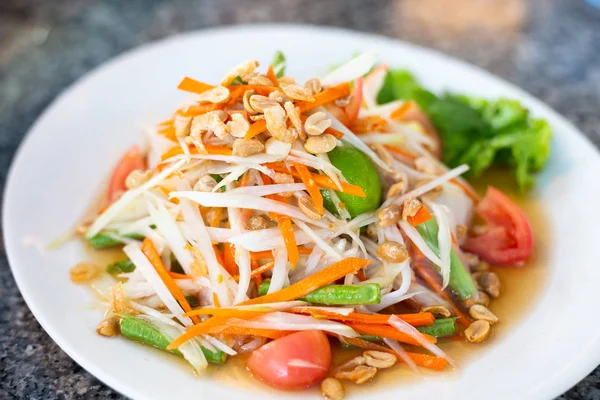 Ahşap bir masada beyaz bir tabak üzerinde Papaya salatası