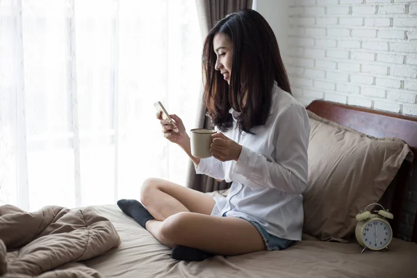 Ázsiai Lány Használ Smartphone Üzenet Tart Csésze Kávét Kezében Ágyán — Stock Fotó