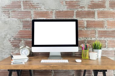 Boş beyaz ekranlı bilgisayar ve ahşap bir masada ofis malzemeleri olan çalışma alanı.